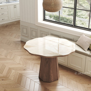 High-angle shot of a modern round sintered stone dining table with a glossy organic-shaped top and a faceted wooden pedestal base, placed on herringbone wood flooring in a bright dining space.